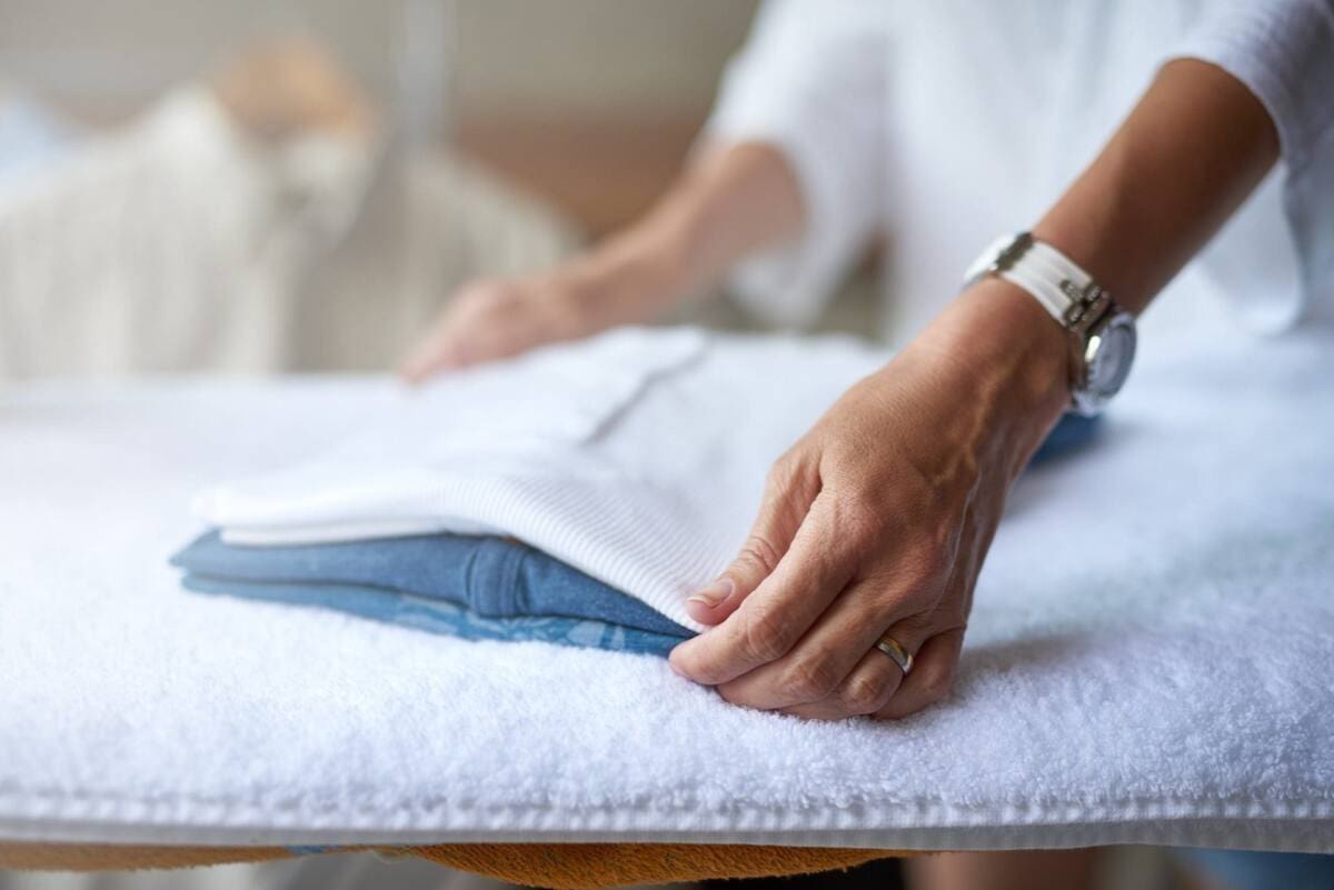 A person folds a white shirt on a padded surface, with visible hands and wristwatch.